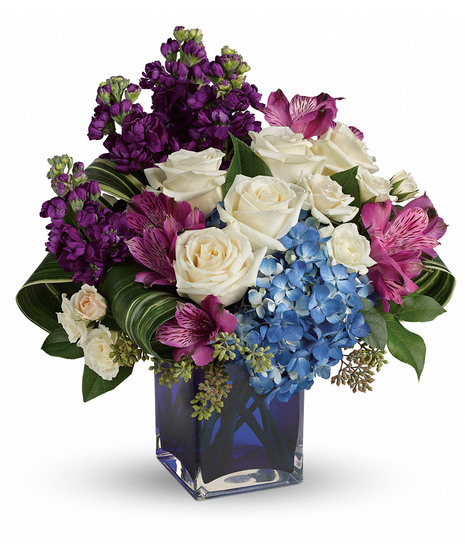 Cobalt blue cube with blue hydrangea, purple stock and alstroemeria, white spray roses, cream roses, salal and aspidistra leaves.